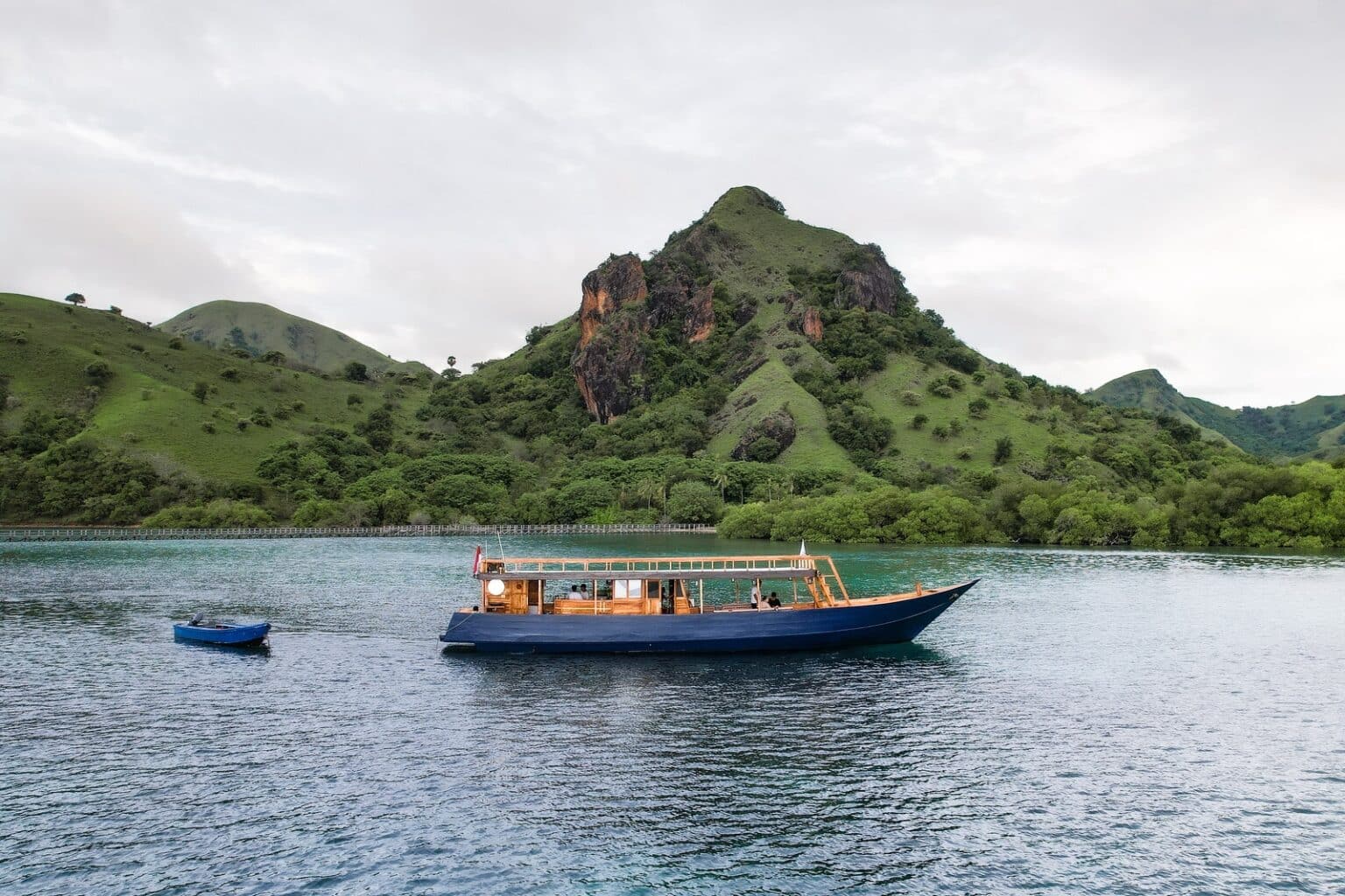 Traditional wooden vessel named Kimochi anchored in a quiet, scenic bay, highlighting the flexible, unhurried pace of a private Komodo boat trip.