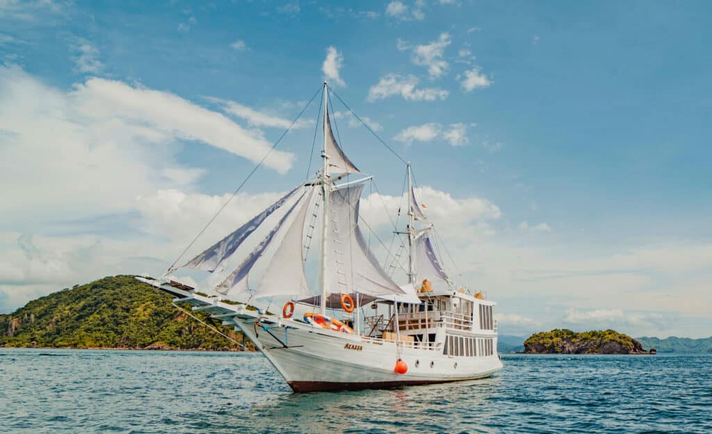 A classic white Phinisi vessel with sails raised, navigating beautiful island waters during a liveaboard private Komodo charter.