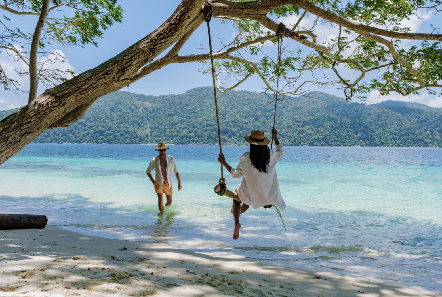 Couple enjoying a secluded island beach of Bidadari Island swing over turquoise waters on an exclusive Labuan Bajo private boat journey.