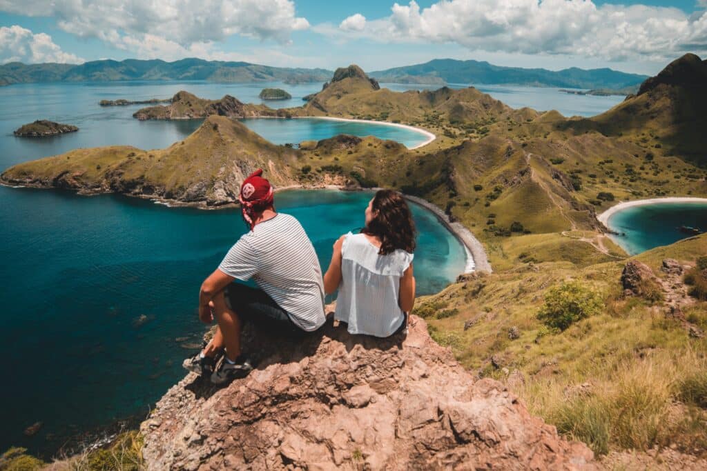 Travelers sitting on a scenic rocky viewpoint of Padar Island overlooking stunning coastal bays, enjoying a fully flexible custom Komodo itinerary.